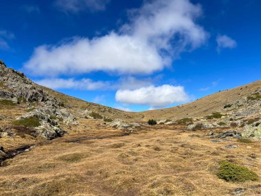 Dağ vadisinde kuru otlar ve dağılmış kayalar bulutlu açık mavi bir gökyüzünün altında