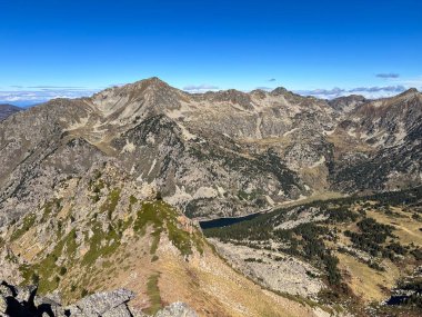 Kayalık tepeleri, bir vadisi, bir gölü ve berrak mavi gökyüzü olan bir dağ sırası.