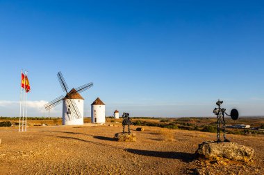 Iconic Cervantes heykelleri ve geleneksel yel değirmenleri açık bir gökyüzü altında La Mancha manzarasına hükmediyorlar.