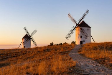 İspanya, Mota del Cuervo 'da bir tepede duran iki geleneksel yel değirmeni gün batımının parlaklığında güneşleniyorlar.