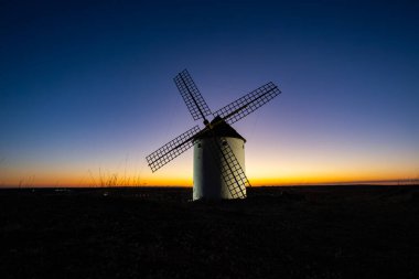 Mota del Cuervo yel değirmeni alacakaranlıkta renkli bir gökyüzüne siluet döküyor.