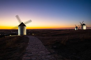 İspanya, Mota del Cuervo 'da renkli bir günbatımı gökyüzüne sahip bir tepede duran yel değirmenleri.