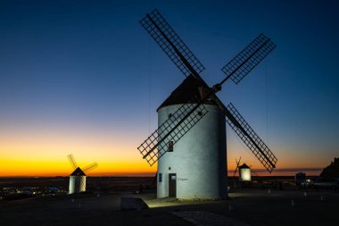 İspanya 'nın Mota del Cuervo şehrinde günbatımı gökyüzünde parlayan tarihi yel değirmenleri.