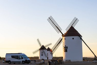 İspanya, La Mancha 'da altın saat gün batımında tarihi yel değirmenlerinin yakınına park edilmiş beyaz karavan.