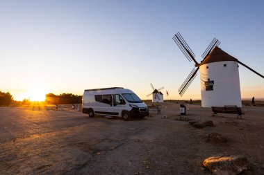 Mancha 'da güzel bir günbatımında ikonik yel değirmenlerinin yanına park edilmiş bir karavan.