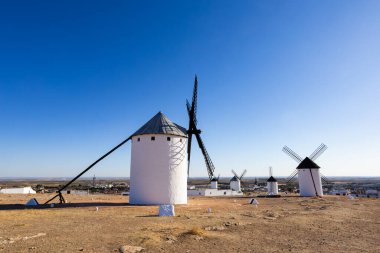 Beyaz tarihi yel değirmenleri, açık mavi gökyüzünün altında kurak araziyi noktalıyor.