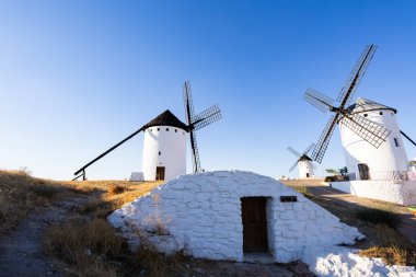 Geleneksel yel değirmenleri, açık mavi gökyüzünün altındaki kuru bir arazide bir tepenin üzerinde duruyorlar.