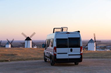 Günbatımında tarihi yel değirmenlerine bakan bir karavan manzaralı bir İspanyol manzarasında park etmiş.