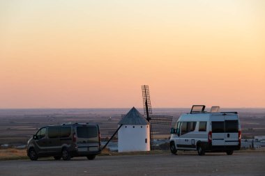 Geleneksel bir İspanyol yel değirmeninin yakınına park etmiş kamp arabaları gün batımında manzarayı seyrediyor.