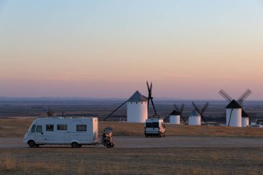 Campo de Criptana, İspanya 'da alacakaranlıkta geleneksel yel değirmenlerine bakan bir tepeye park edilmiş motorlu araçlar.