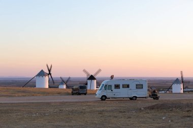 Gün batımında La Mancha 'da ikonik beyaz yel değirmenlerine hayran olan bir kamp aracı park etti.