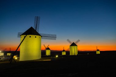 La Mancha 'da renkli bir alacakaranlık karşısında parlayan tarihi İspanyol yel değirmenleri.
