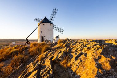 Beyaz yel değirmenleri Consuegra, La Mancha 'nın kayalık arazisinde altın güneş ışığını yakalıyorlar.