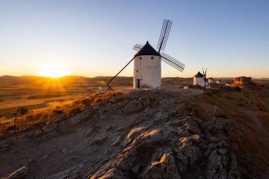 Geleneksel İspanyol yel değirmenleri ve sıcak günbatımı ışığında yıkanmış eski bir kale durağı.