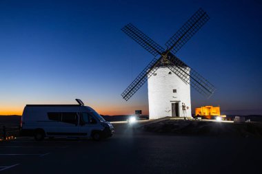 İspanya, Consuegra 'da alacakaranlıkta klasik bir İspanyol yel değirmeninin yanına park edilmiş bir karavan.