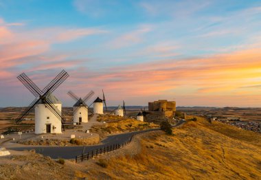 Yel değirmenleri ve Consuegra kalesi renkli bir günbatımında bir tepenin üzerinde duruyor.