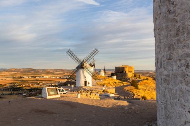 İspanya, La Mancha 'da gün batımında tarihi yel değirmenleri ve şato bir tepenin üzerinde beliriyor.
