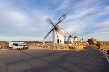 İspanya 'nın Consuegra kentindeki bir tepede tarihi yel değirmenlerinin ve kalenin yakınına park edilmiş bir karavan.
