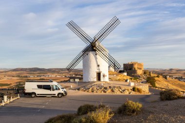 İspanya 'nın Consuegra kentindeki bir tepede tarihi yel değirmenlerinin ve kalenin yakınına park edilmiş bir karavan.