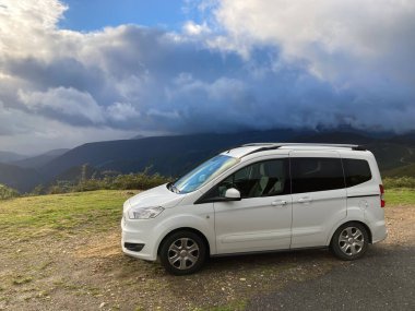 İspanya, Asturias üzerinde dramatik bir gökyüzü olan bir dağ yolunda dinlenen beyaz bir araç.