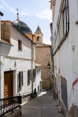 Alcala Del Jucar, İspanya; 20 Eylül 2025: Dar cadde, kilise çan kulesine çıkan beyaz binalardan aşağı sarkıyor