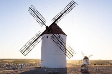 Mota del Cuervo, İspanya; 21 Eylül 2025: Bir çocuk tarafından izlenen altın gün batımında tepede duran geleneksel İspanyol yel değirmenleri