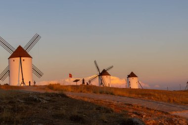 Mota del Cuervo, İspanya; 21 Eylül 2025: İspanya 'nın La Mancha kentinde gün batımında altın bir gökyüzüne karşı yel değirmenleri silueti