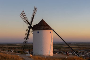Mota del Cuervo, İspanya; 21 Eylül 2025: Gün batımında La Mancha manzarasına bakan bir tepede duran yel değirmeni
