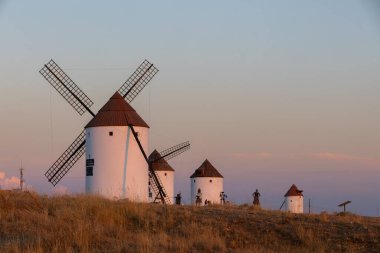 Mota del Cuervo, İspanya; 21 Eylül 2025: Renkli bir akşam gökyüzünde heykeli olan bir tepede duran çok sayıda İspanyol yel değirmeni