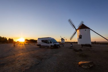 Mota del Cuervo, İspanya; 22 Eylül 2025: Kamp aracı altın saatinde tarihi yel değirmenlerinin yakınına park edilmiş, seyahat etmenin özünü yakalıyor