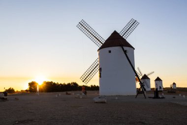 Mota del Cuervo, İspanya; 22 Eylül 2025: Batan güneşle birlikte platoda duran tarihi yel değirmenleri sıcak bir parıltı yaratıyor
