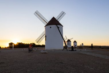 Mota del Cuervo, İspanya; 22 Eylül 2025: Bisikletçi, İspanya 'nın La Mancha kentinde günbatımında geleneksel yel değirmenlerinin önünden geçiyor.