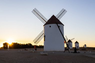 Mota del Cuervo, İspanya; 22 Eylül 2025: Mota del Cuervo 'da canlı bir günbatımı gökyüzünün altında duran beyaz yel değirmenleri