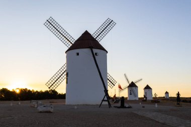 Mota del Cuervo, İspanya; 22 Eylül 2025: İspanya 'da gün batımında berrak bir gökyüzüne karşı siluette görünen geleneksel yel değirmenleri
