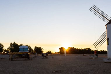 Mota del Cuervo, İspanya; 22 Eylül 2025: Kamp aracı gün batımında tarihi bir rüzgar değirmeninin yakınına park edilmiş, seyahat ve özgürlüğü vurguluyor