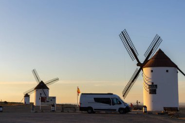 Mota del Cuervo, İspanya; 22 Eylül 2025: Kamp aracı Mota del Cuervo 'da sıcak günbatımında tepedeki ikonik beyaz yel değirmenlerine hayran kaldı