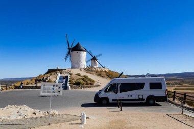 Consuegra, İspanya; 23 Eylül 2025: Konsuegra 'da güneşli bir günde tarihi yel değirmenlerine bakan kamp aracı