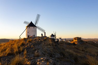 Consuegra, İspanya; 23 Eylül 2025: Konsuegra, İspanya 'da gün batımında bir tepenin üzerinde duran yel değirmenleri ve bir kale