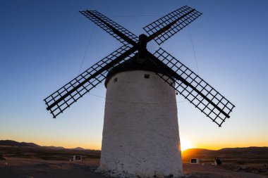 Consuegra, İspanya; 23 Eylül 2025: Geleneksel İspanyol yel değirmeni canlı bir günbatımı gökyüzüne karşı bir tepede duruyor