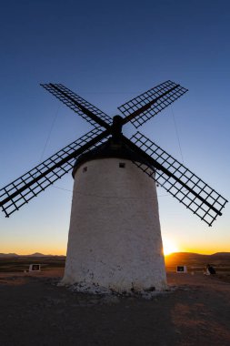Consuegra, İspanya; 23 Eylül 2025: Geleneksel İspanyol yel değirmeni batan güneşin canlı renklerine karşı gururla ayakta duruyor
