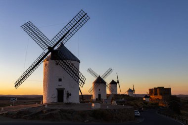 Consuegra, İspanya; 23 Eylül 2025: Geleneksel yel değirmenleri ve İspanya 'nın La Mancha kentinde canlı bir günbatımına karşı tarihi kale silueti