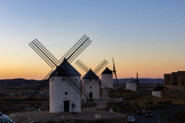 Consuegra, İspanya; 23 Eylül 2025: Bir tepenin üzerinde duran yel değirmenleri alacakaranlıkta tarihi bir La Mancha manzarası yaratıyor