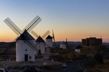 Consuegra, İspanya; 23 Eylül 2025: Beyaz yel değirmenleri ve Consuegra 'da günbatımında tepede duran tarihi bir kale