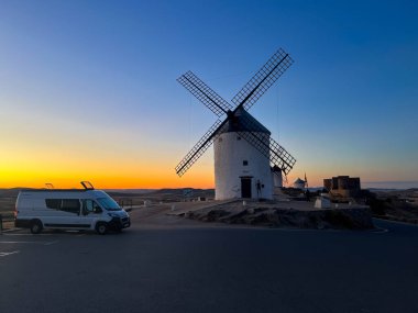 Consuegra, İspanya; 23 Eylül 2025: Campervan, Consuegra 'daki güzel günbatımında tarihi yel değirmenleri ve kalenin yakınına park etti