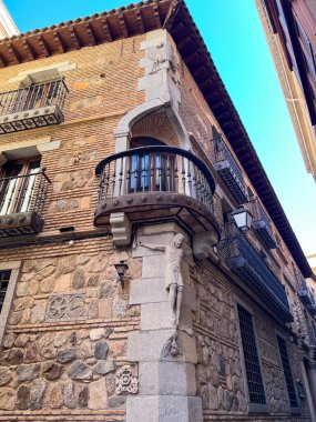 Toledo, İspanya; 24 Eylül 2025: İspanya 'nın Toledo kentinde haç heykeli, karmaşık taş işçiliği ve balkonlarla tarihi yapı cephesi