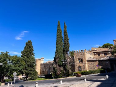 Toledo, İspanya; 24 Eylül 2025: Geleneksel taş duvarları ve belirgin selvi ağaçları ile temiz bir gökyüzü altında eski kasaba mimarisi