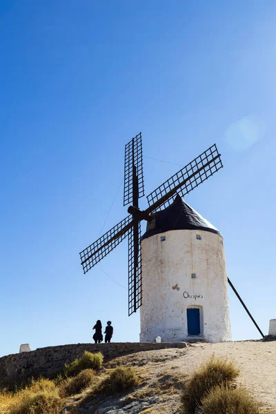 Consuegra, İspanya; 23 Eylül 2025: İnsanlar bir tepede durmuş, açık mavi gökyüzünün altındaki antika bir yel değirmenine hayran bakıyorlar.