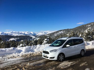 Alp, İspanya; 8 Şubat 2018: Açık mavi gökyüzünün altındaki kış dağlarına bakan karlı bir yola park edilmiş beyaz modern minibüs