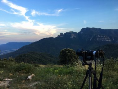 Vall d 'en Bas, İspanya; 27 Temmuz 2018: La Vall d' en Bas 'da alacakaranlıkta doğal bir dağ vadisine bakan bir tripoda telefoto lensli kamera