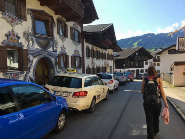 Garmisch-Partenkirchen, Almanya; 16 Ağustos 2018: Ballengasse 'de boyalı freskler ve park halindeki arabalarla geleneksel Bavyera evlerinin önünden geçen kadın
